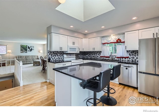 kitchen with appliances with stainless steel finishes, a sink, dark countertops, a breakfast bar, and light wood-type flooring