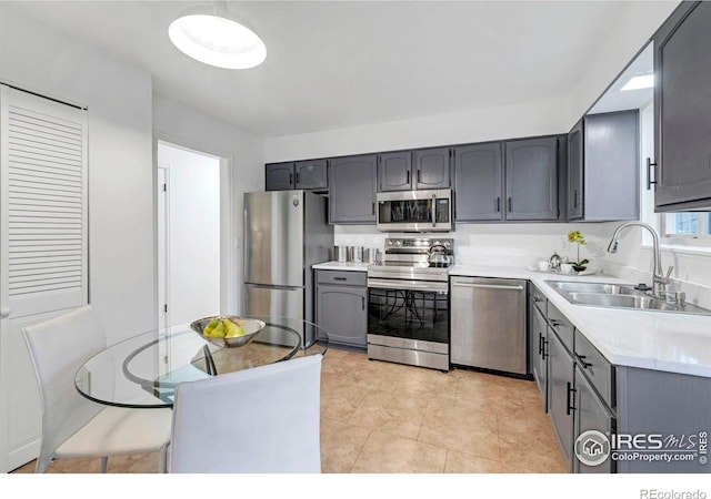 kitchen featuring appliances with stainless steel finishes, a sink, gray cabinets, and light countertops