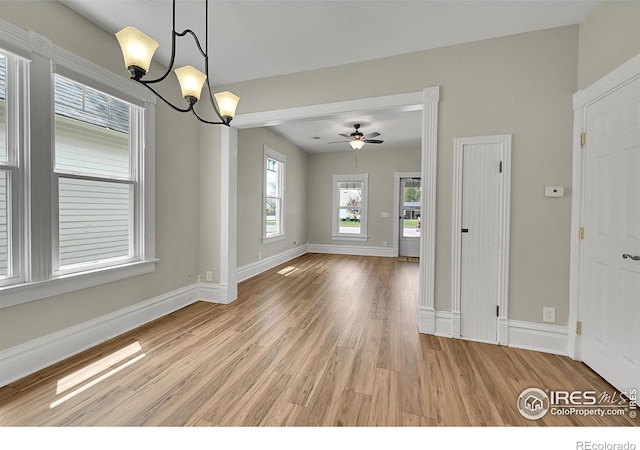 unfurnished dining area with light wood-type flooring, a chandelier, baseboards, and a ceiling fan