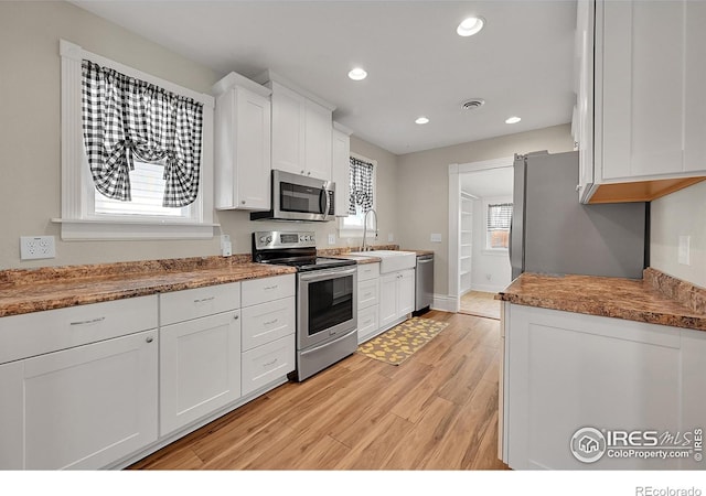 kitchen with stainless steel appliances, white cabinets, light wood-style flooring, recessed lighting, and a sink