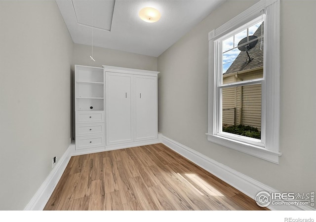 unfurnished bedroom featuring attic access, light wood-style flooring, and baseboards