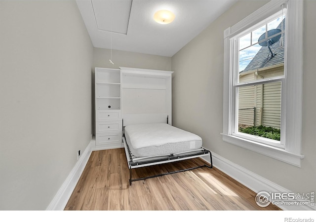 bedroom featuring attic access, light wood finished floors, baseboards, and multiple windows