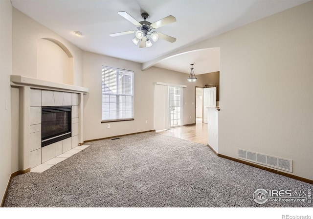 unfurnished living room featuring carpet floors, a tiled fireplace, baseboards, and ceiling fan