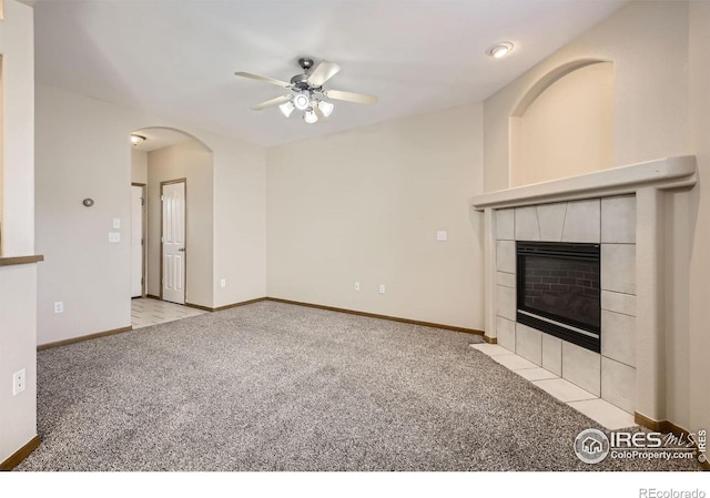 unfurnished living room featuring a ceiling fan, carpet floors, a tile fireplace, and baseboards