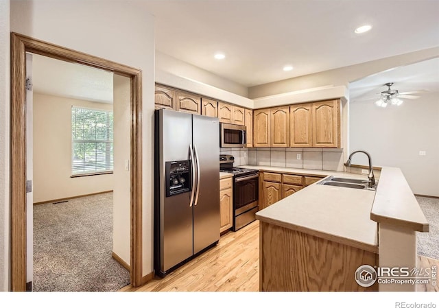kitchen featuring stainless steel appliances, a sink, a peninsula, light countertops, and a ceiling fan