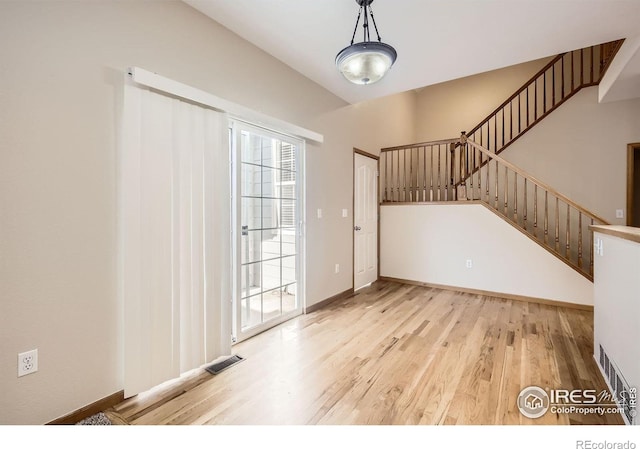 unfurnished living room with light wood-type flooring, stairs, and baseboards