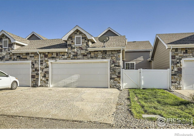 view of front of property featuring stone siding, fence, driveway, and a shingled roof