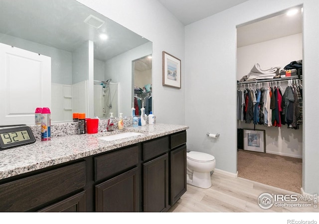 bathroom featuring a walk in closet, a shower stall, vanity, wood finished floors, and toilet