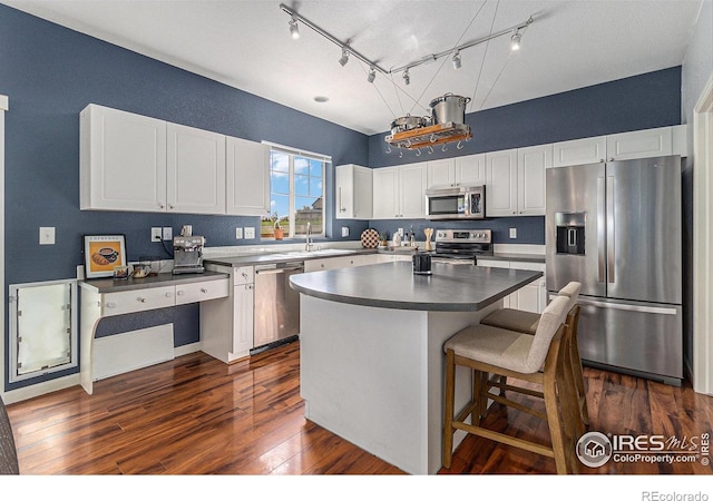 kitchen featuring stainless steel appliances, white cabinets, dark wood-type flooring, a center island, and dark countertops