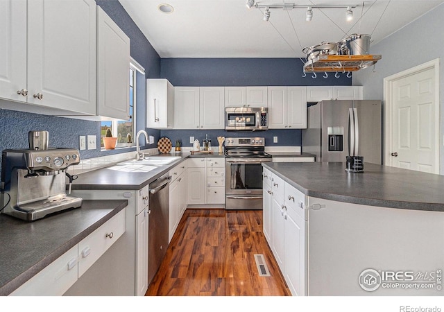 kitchen with stainless steel appliances, dark countertops, dark wood-style flooring, white cabinets, and a sink