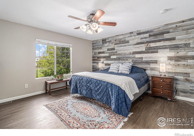 bedroom with an accent wall, wood walls, wood finished floors, baseboards, and ceiling fan