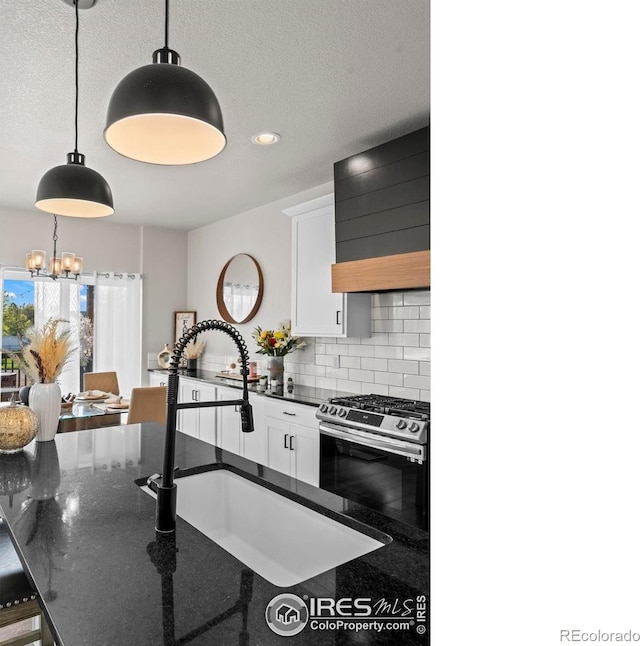 kitchen with stainless steel gas range oven, a sink, a chandelier, decorative backsplash, and wall chimney range hood