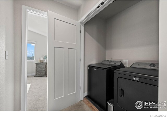 clothes washing area with washing machine and clothes dryer, light colored carpet, and baseboards