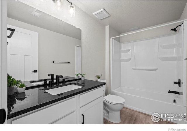 full bath with wood finished floors, toilet, vanity,  shower combination, and a textured ceiling