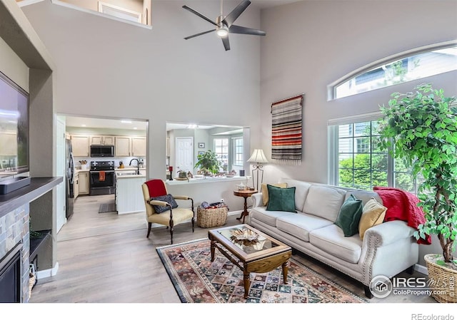 39 Sebring Ln, Johnstown, CO 80534 - living area featuring light wood-type flooring, healthy amount of natural light, ceiling fan, a towering ceiling, and a glass covered fireplace