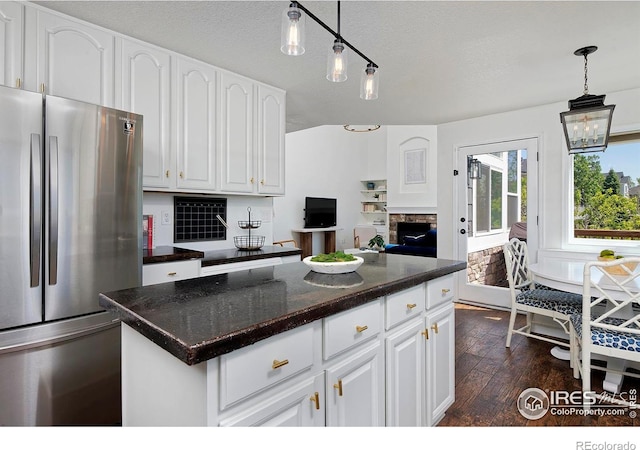 kitchen with freestanding refrigerator, dark wood-type flooring, dark countertops, a stone fireplace, and a textured ceiling