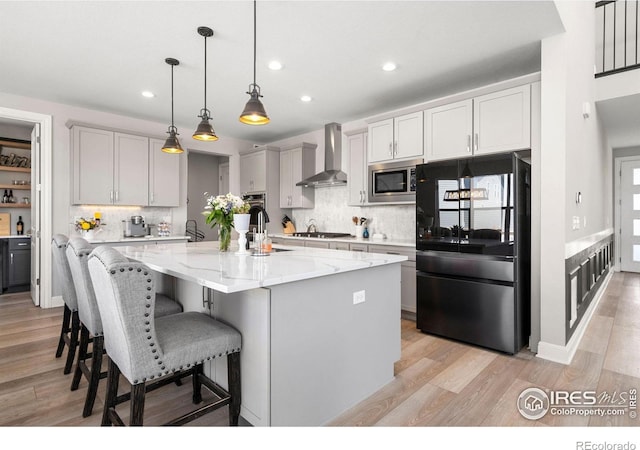 5085 Blanchette St, Timnath, CO 80547 - kitchen featuring appliances with stainless steel finishes, wall chimney range hood, recessed lighting, light wood-style flooring, and light stone counters