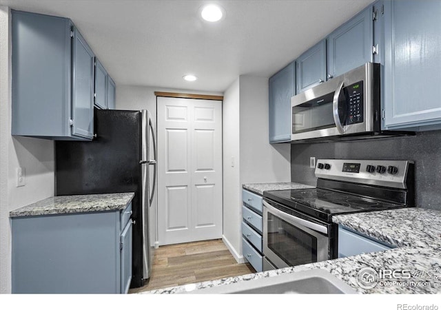 7820 W 87th Dr Unit K, Arvada, CO 80005 - kitchen featuring stainless steel appliances, blue cabinets, light wood finished floors, recessed lighting, and light stone countertops
