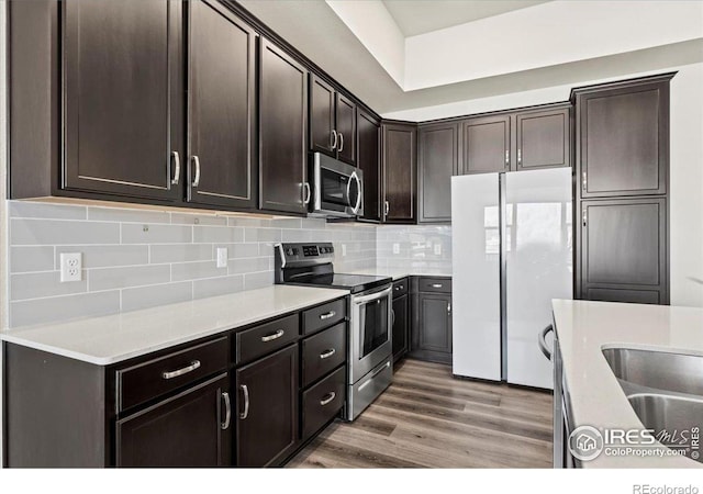 350 High Point Dr Unit 201, Longmont, CO 80504 - kitchen with stainless steel appliances, dark brown cabinets, decorative backsplash, light wood-style floors, and light countertops