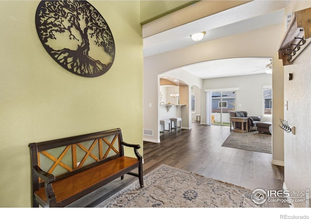 corridor with arched walkways, wood finished floors, and baseboards