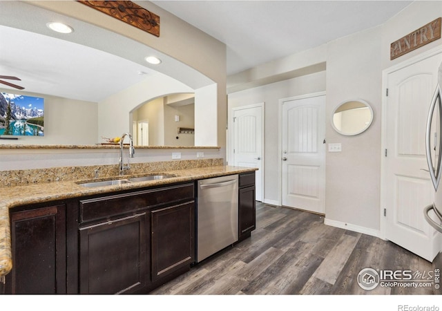 kitchen with appliances with stainless steel finishes, a sink, light stone countertops, dark brown cabinets, and dark wood-type flooring