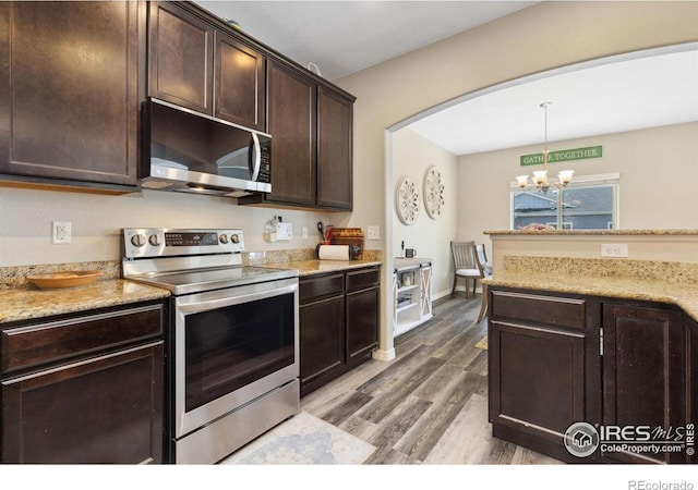kitchen with stainless steel appliances, a chandelier, dark brown cabinets, wood finished floors, and decorative light fixtures