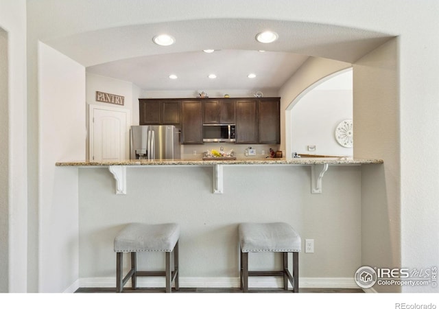 kitchen with appliances with stainless steel finishes, dark brown cabinets, baseboards, a breakfast bar area, and recessed lighting