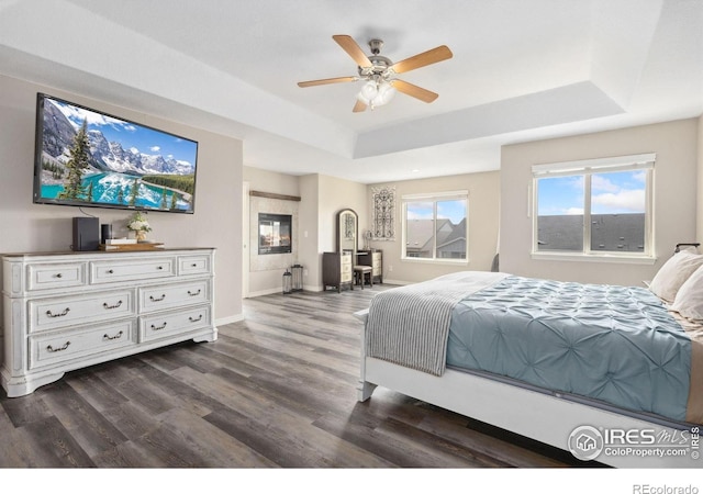 bedroom with a tray ceiling, dark wood finished floors, baseboards, and a ceiling fan
