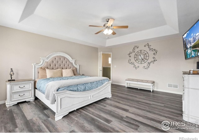 bedroom featuring a tray ceiling, wood finished floors, baseboards, and ceiling fan
