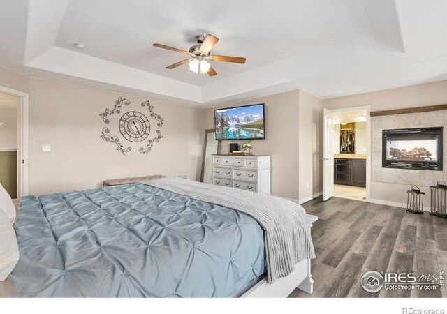 bedroom featuring a tray ceiling, dark wood-style flooring, baseboards, and ensuite bath