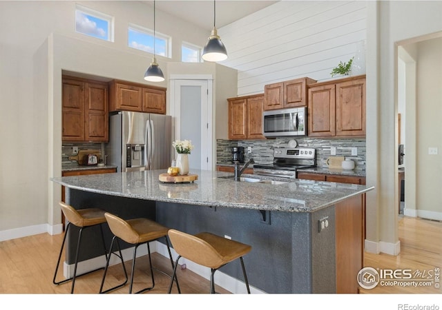 2119 Pelican Farm Rd, Windsor, CO 80550 - kitchen featuring stainless steel appliances, light wood-style floors, backsplash, a high ceiling, and a kitchen breakfast bar