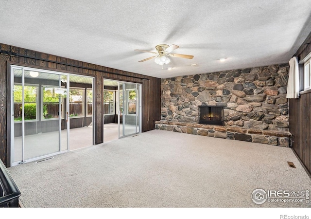 1320 Lory St, Fort Collins, CO 80524 - unfurnished living room with ceiling fan, carpet floors, wooden walls, a textured ceiling, and a stone fireplace