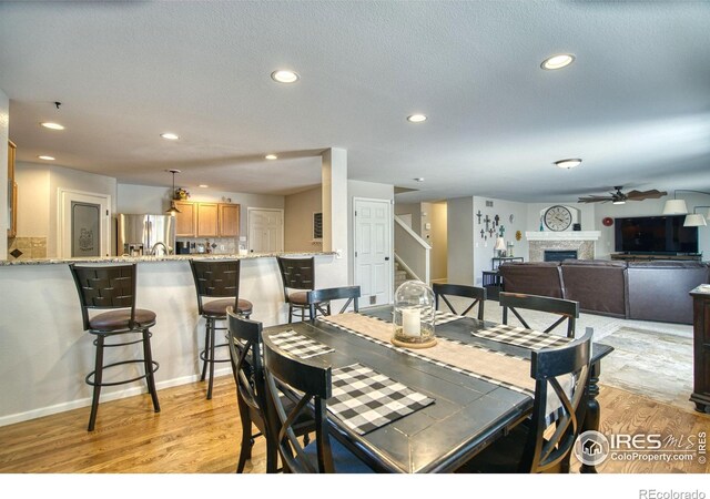 dining room featuring stairs, ceiling fan, light wood finished floors, a fireplace, and recessed lighting