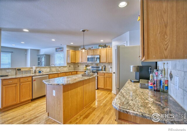 kitchen with stainless steel appliances, a sink, a kitchen island, decorative backsplash, and light wood-style floors