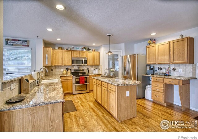 kitchen featuring appliances with stainless steel finishes, a sink, light stone counters, a textured ceiling, and light wood finished floors
