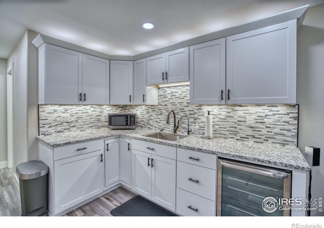 kitchen with wine cooler, a sink, light wood finished floors, stainless steel microwave, and tasteful backsplash
