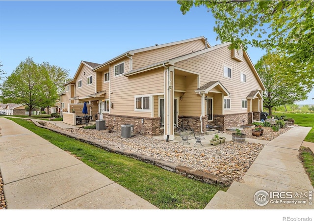 view of front facade featuring a patio, central AC, a residential view, and brick siding