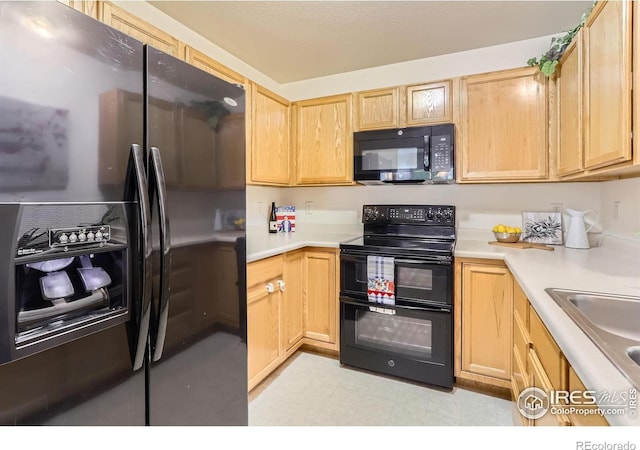 kitchen with black appliances, a sink, light countertops, light brown cabinetry, and light flooring