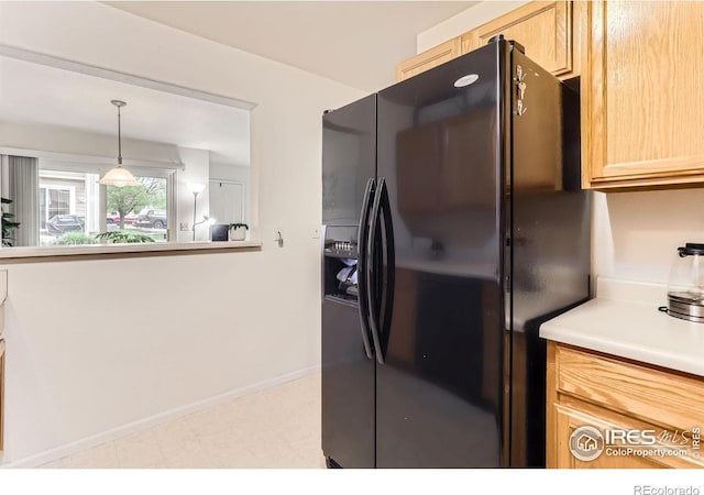 kitchen with black fridge with ice dispenser, light countertops, light brown cabinetry, baseboards, and hanging light fixtures