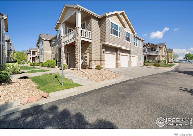 view of front of property with an attached garage, a balcony, a residential view, driveway, and stone siding