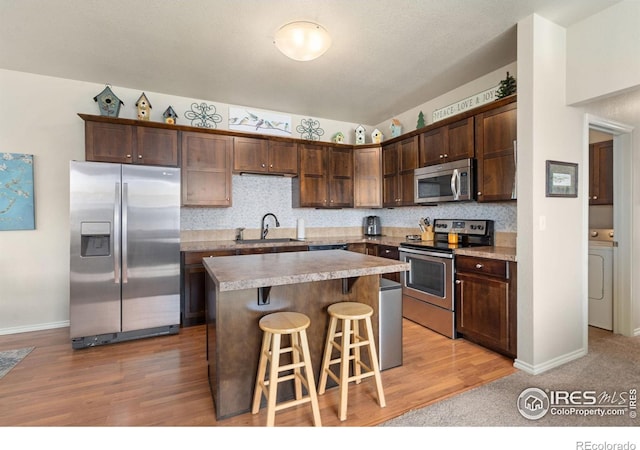 kitchen featuring appliances with stainless steel finishes, washer / clothes dryer, a kitchen bar, dark brown cabinetry, and a sink