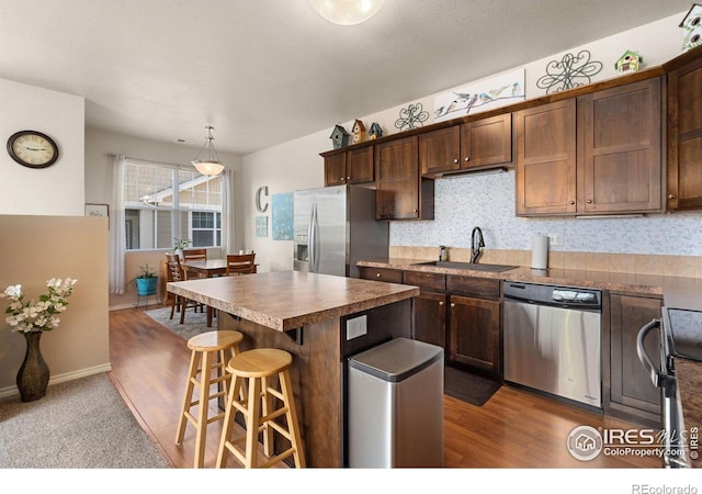 kitchen featuring a sink, stainless steel appliances, a breakfast bar area, a center island, and dark wood-type flooring