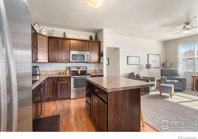 kitchen featuring stainless steel appliances, open floor plan, a kitchen island, light wood-style flooring, and a ceiling fan