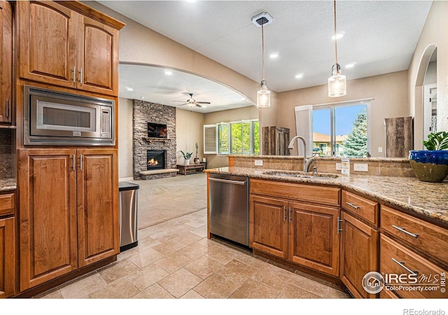 4609 Freehold Dr, Windsor, CO 80550 - kitchen with appliances with stainless steel finishes, ceiling fan, a stone fireplace, light stone countertops, and brown cabinetry