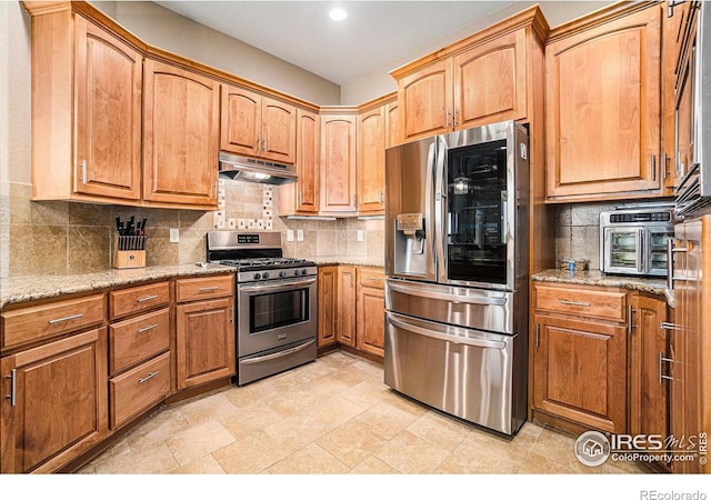 4609 Freehold Dr, Windsor, CO 80550 - kitchen featuring appliances with stainless steel finishes, under cabinet range hood, decorative backsplash, light stone countertops, and recessed lighting