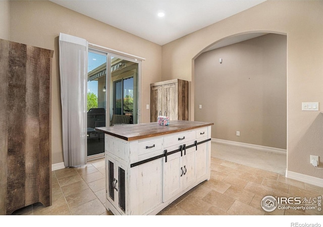 4609 Freehold Dr, Windsor, CO 80550 - kitchen with wooden counters, arched walkways, white cabinetry, and light stone finish flooring