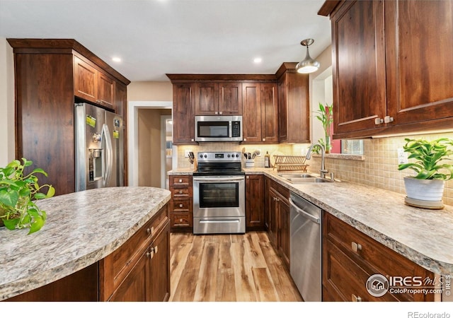 kitchen featuring appliances with stainless steel finishes, a sink, light wood-style floors, tasteful backsplash, and light countertops