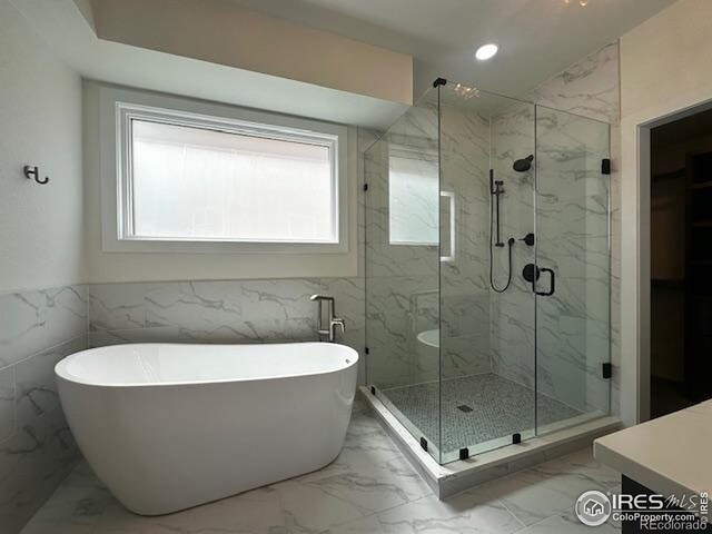 410 Superior Dr, Superior, CO 80027 - full bathroom featuring healthy amount of natural light, marble look tile flooring, a freestanding bath, a marble finish shower, and tile walls