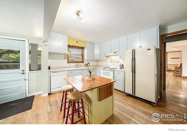 kitchen featuring white appliances, under cabinet range hood, light wood-style floors, and plenty of natural light