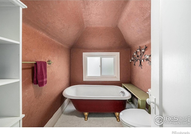 full bathroom with lofted ceiling, a freestanding bath, toilet, a textured wall, and baseboards